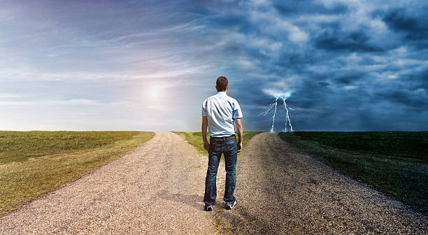Concept of personal decision making. Man stand at a forked road and has to choose his way forward. The one to left is covered in sunlight. The one to the right is dark and lightning is in the horizon.